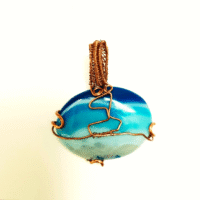 Set course for adventure with this one-of-a-kind handcrafted pendant. A piece of dyed blue agate, rich with swirling ocean hues, forms the backdrop for a miniature sailing ship sculpted from reclaimed copper. The contrast between the stone’s cool, watery blues and the warm patina of upcycled copper brings the piece to life—evoking a vessel embarking on its next great journey. The agate’s natural banding resembles distant waves or a shifting horizon, while the carefully detailed ship adds a touch of wanderlust and storytelling. Perfect for ocean lovers, explorers at heart, or anyone drawn to jewellery with meaning, this pendant is more than an accessory — it’s a reminder that there’s always another horizon waiting. Wear a piece which sails with you on your next adventure.